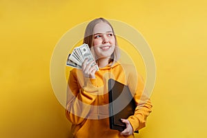 portrait of young exciting smiling pretty woman holding a stack of money dollar bills and laptop. Teenager Girl dreaming