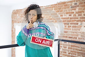 Portrait of a young and exotic woman begging for silence. She holds in her hand a sign with the text On Air