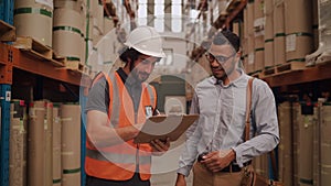 Portrait of young factory logistic worker signing papers on clipboard standing with business person in the warehouse