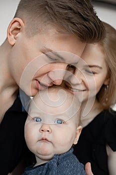 Portrait of young good-looking family in dark clothes with plump cherubic baby infant toddler kiss on white background. photo