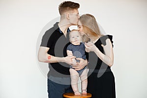Portrait of young family in dark clothes with plump cherubic baby infant toddler standing, kissing on white background. photo