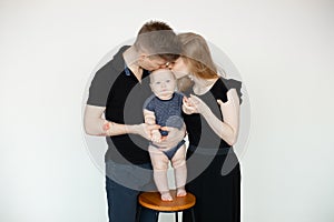 Portrait of young family in dark clothes with plump cherubic baby infant toddler standing, kissing on white background. photo