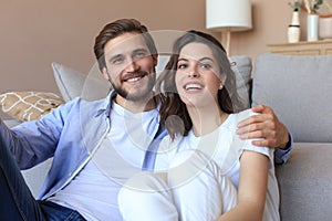 Portrait young family of happy husband and wife sitting in sofa cuddle looking at camera posing