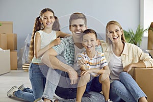 Portrait of young family hugging and smiling while sitting on floor in living room.