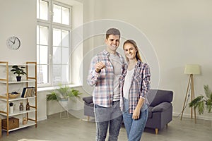 Portrait of a happy young family with keys standing in the living room in their new house
