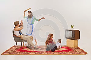 Portrait of young family watching TV isolated over grey background. Kids watching cartoons, man and woman quarreling