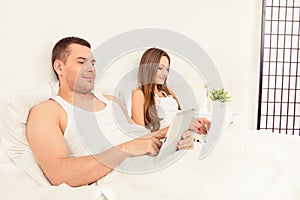 Portrait of young family working in bed with tablet and laptop