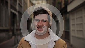 Portrait of a young fashionable handsome guy smiling at the camera on the street of an old European town. Slow motion