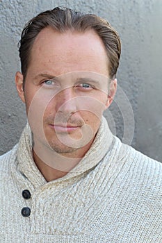 Portrait of young fashionable male model in trendy beige sweater posing over gray background. Close up. Studio shot