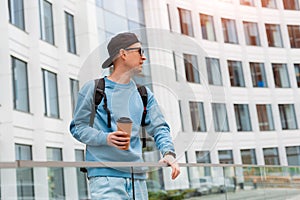 Portrait young fashionable man in casual clothes with coffee and sunglasses background of a white office building