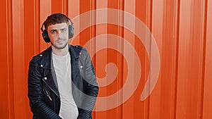 Portrait of young fashionable positive man in earphones or headphones near orange wall background