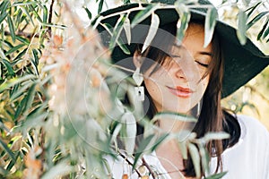 Portrait of young fashionable woman with modern earrings posing in  green olive branches in soft evening light, stylish boho girl