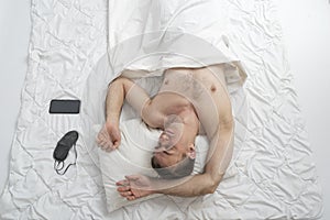 Portrait of young fast-sleeping man, top view. Sound sleep. Guy sleeps on white cotton bed linen