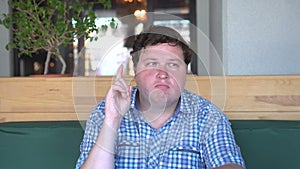 Portrait of a young fat man having idea and pointing finger up in cafe or restaurant