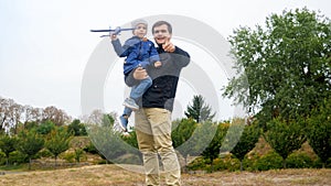 Portrait of young father holding his little son and teaching throwing toy airplane at park