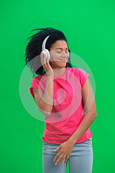 Portrait of young female African American dancing and enjoying music in big white headphones. Black woman with curly