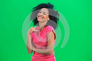 Portrait of young female African American flirtatious smiling. Black woman with curly hair in pink tshirt poses on green