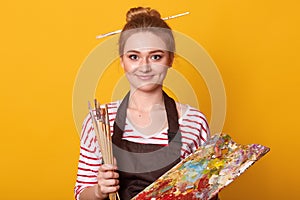 Portrait of young female artist holding brushes and mix color oil painting on palette, attractive woman painter wearing striped