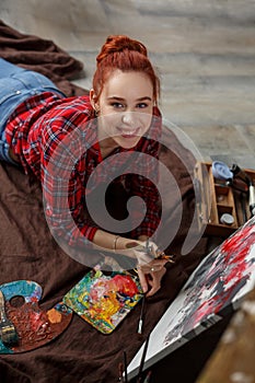 Portrait of a young female artist painting. Smiling girl with a palette in her hands and looking at the camera