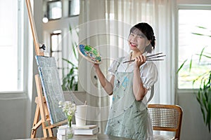 Portrait of a young female artist working on an abstract acrylic canvas painting in an art painting studio.