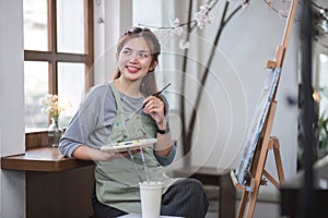 Portrait of a young female artist working on an abstract acrylic canvas painting in an art painting studio.