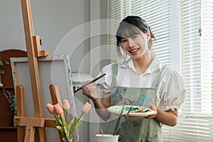 Portrait of a young female artist working on an abstract acrylic canvas painting in an art painting studio.
