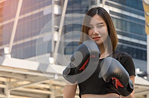 Portrait of young female boxer in black boxing gloves standing in front of modern building