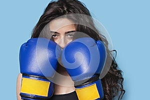 Portrait of a young female boxer with fists up against blue background