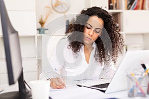 Portrait of young female business employee writing and working with laptop