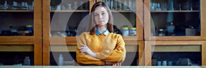 Portrait of young female college student in chemistry class, sitting behind the desk with crossed arms.