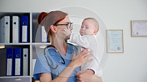 portrait of a young female doctor in glasses holding a small child in her arms in a medical office, smiling and looking