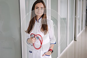 Portrait young female doctor holding a stethoscope in hands. Bright clinic