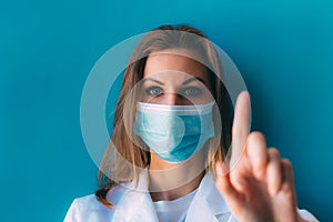 Portrait of young female doctor in medical mask and white gown on blue background.