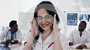 Portrait of young female doctor putting stethoscope on the neck with team of staff on the background in hospital.