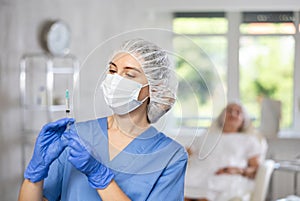 Portrait of young female doctor in scrub and mask holding syringe.