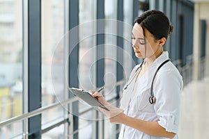 Portrait of young female doctor standing in hospital corridor. Caucasian woman working in nursing home.