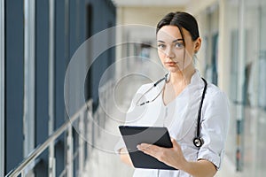 Portrait of young female doctor standing in hospital corridor. Caucasian woman working in nursing home.