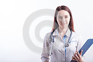 Portrait of a young female doctor in a white uniform with a folder in hands in the studio on a white background with copyspace.