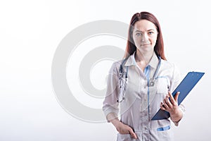 Portrait of a young female doctor in a white uniform with a folder in hands in the studio on a white background with copyspace.