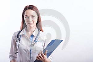 Portrait of a young female doctor in a white uniform with a folder in hands in the studio on a white background with copyspace.