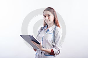 Portrait of a young female doctor in a white uniform with a folder and a pen in hands in the studio on a white background.