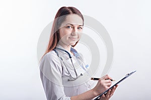 Portrait of a young female doctor in a white uniform with a folder and a pen in hands in the studio on a white background.