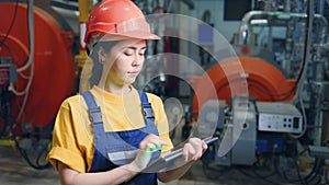 Portrait of a young female engineer wearing a protective helmet records the meter reading on a tablet and smiles. Modern