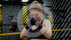 Portrait of a young female kickboxer in the gym with black bandages on her hands