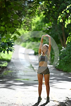 Portrait of young female runner stretching arms before running at morning.