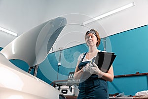 Portrait of young female smiling mechanic with documents in auto repair shop. Bottom view. The concept of women& x27;s