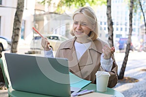 Portrait of young female student, modern woman in outdoor coffee shop, street cafe, talking to someone via laptop, video