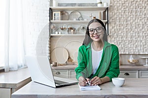 Portrait of a young female student who studies remotely with a laptop. Sitting in the kitchen at the table with a