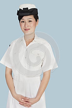 Portrait of a young female US Navy officer standing with hands clasped over light blue background