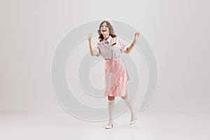 Portrait of young female waitress, sensual woman in retro american fashion style of 70s, 80s in action motion over grey